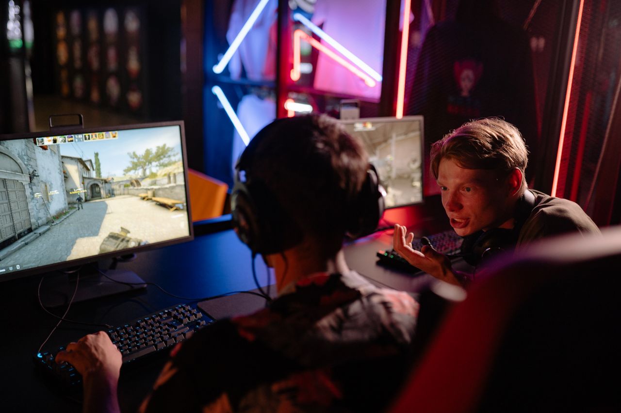 Two gamers engaged in a heated video game session surrounded by neon lights and computer screens.
